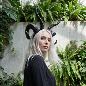 May include: A black headpiece featuring multiple curved, textured horns extending upward and outward from a central band. The horns have a glossy finish and a spiraled, ridged surface structure, creating a dramatic silhouette above the head.