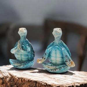 May include: Two blue and green ceramic turtle figurines in a yoga pose. The turtles are sitting on a wooden surface.