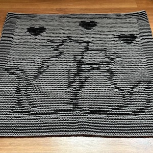 Puede incluir: Manta de punto negra y blanca con un diseño geométrico y tres corazones.