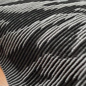 May include: Close-up of a gray and white textured fabric with a ribbed pattern. The fabric appears to be soft and woven, with alternating dark and light gray stripes. The texture is visible, creating a sense of depth.