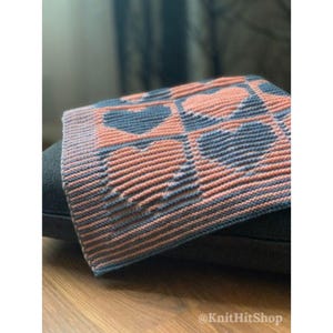 May include: A knitted blanket featuring a repeating pattern of hearts in alternating peach and slate blue colors. The textile has a textured, ribbed stitch construction with a consistent grid layout. The text KnitHitShop is visible in the corner.