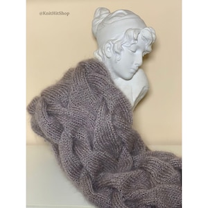 Peut inclure: Une écharpe tricotée de couleur mauve avec un motif de torsades proéminent, drapée sur un buste de style classique blanc. Le texte KnitHitShop est visible dans le coin supérieur gauche de l'image, affiché dans une police simple.