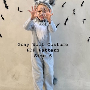 Könnte beinhalten: Ein graues Wolfskostüm bestehend aus einem langärmeligen Overall mit weißem, flauschigem Brustbereich, einer passenden Kapuze mit Kunstfellohren und einem Schwanz. Der Text Gray Wolf Costume PDF Pattern Size 6 ist in Schwarz auf dem Kostüm aufgedruckt.
