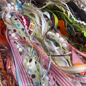 May include: A colorful assortment of ribbons, trims, and decorative elements. The image features a variety of textures, including striped, polka-dotted, and solid ribbons in shades of pink, blue, green, and orange. Some ribbons have pom-poms and lace.