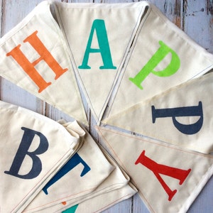 May include: A white fabric banner with the word "HAPPY" spelled out in colorful letters. The letters are in different colors, including orange, green, blue, and red. The banner is strung together with string and is perfect for a birthday party or other celebration.