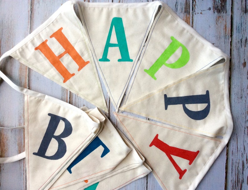 May include: A white fabric banner with the word "HAPPY" spelled out in colorful letters. The letters are in different colors, including orange, green, blue, and red. The banner is strung together with string and is perfect for a birthday party or other celebration.