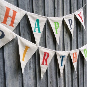 May include: A white fabric banner with the words "Happy Birthday" in colorful letters. The letters are in different colors, including red, orange, yellow, green, blue, and purple.
