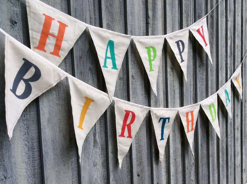 May include: A white fabric banner with the words "Happy Birthday" in colorful letters. The letters are in different colors, including red, orange, yellow, green, blue, and purple.