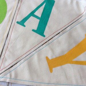 May include: A close-up of a fabric banner with the letters "DAY" sewn together. The "D" is green, the "A" is teal, and the "Y" is yellow.