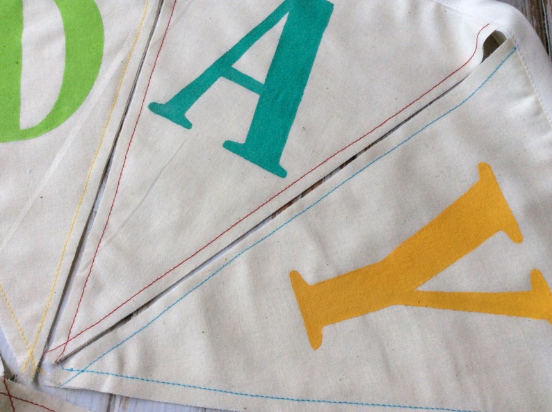 May include: A close-up of a fabric banner with the letters "DAY" sewn together. The "D" is green, the "A" is teal, and the "Y" is yellow.