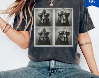 May include: Dark gray t-shirt featuring a four-panel image of a rooster wearing sunglasses. The rooster is in black and white. The word "Pepper" is at the bottom of the image. The shirt is worn by a person.