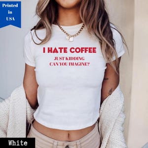 Puede incluir: Top corto blanco con el texto rojo "I HATE COFFEE JUST KIDDING CAN YOU IMAGINE?". La camiseta está hecha de un material suave y lleva las etiquetas "Printed in USA" y "White".