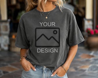 May include: A charcoal gray short-sleeve crewneck t-shirt featuring a black graphic of a mountain landscape inside a rectangular frame with the text YOUR DESIGN printed in a sans-serif font above and below the graphic element.