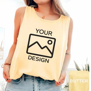May include: A light yellow sleeveless tank top featuring a black graphic print on the front. The graphic consists of the text "YOUR" above a rectangular icon of a mountain landscape and the sun, with the word "DESIGN" printed below the icon.