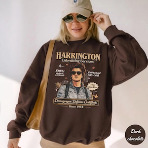 May include: Dark chocolate brown sweatshirt with the text "HARRINGTON Babysitting Services" and an image of a man wearing sunglasses. The sweatshirt also includes the text "Demogorgon Defense Certified! Since 1984."