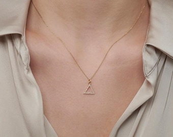 May include: A delicate gold chain necklace featuring a small, open triangle pendant. The pendant is encrusted with tiny, clear, sparkling stones along its three sides, suspended from a thin, polished gold-tone metal chain that rests against the neck.