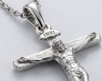 May include: A silver-toned metal crucifix pendant on a matching chain. The pendant features a detailed figure of a person on a cross with a textured surface. Above the figure, a small plaque is engraved with the letters INRI in capital letters.