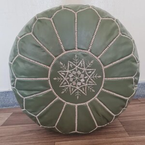 Pode incluir: Puff redondo de couro verde-oliva com um padrão geométrico. O puff apresenta um design central bordado e costuras decorativas ao longo das costuras. Esta almofada de chão adiciona um toque boêmio a qualquer espaço.