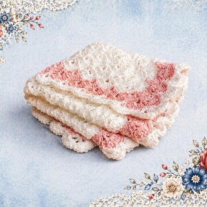May include: A stack of three white and pink crocheted baby blankets. The blankets have a scalloped edge and a pink border. The background is a light blue with floral and lace accents.