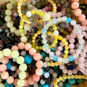 Puede incluir: Una colección de pulseras de cuentas en varios colores, incluyendo rosa, amarillo, verde, azul y negro. Las cuentas son redondas y parecen ser de piedra o vidrio. Las pulseras están enredadas, creando una exhibición colorida.