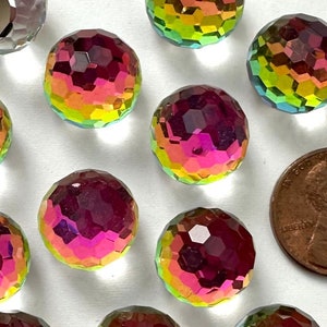 May include: A collection of faceted, iridescent glass beads in shades of pink, purple, yellow, and green. One bead is silver. A penny is included for size comparison. The beads have a spherical shape and a cut-glass appearance.