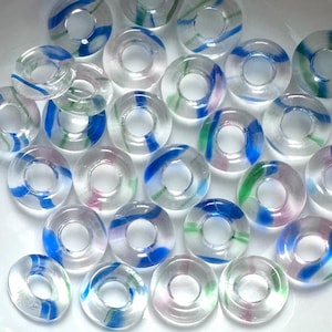 May include: A selection of clear, circular glass beads with colourful, swirled patterns. The beads have blue, green, and pink accents, creating a vibrant look. The beads are presented in a white bowl.