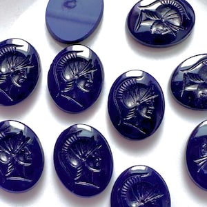 May include: Ten dark blue oval-shaped glass cabochons with a carved design of a warrior's head in profile.