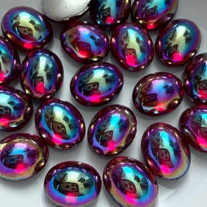 May include: A collection of oval-shaped cabochons with a reflective, iridescent finish that shifts between deep purple, magenta, and bright cyan tones. One cabochon is flipped over to reveal a smooth, matte silver-colored flat back surface.