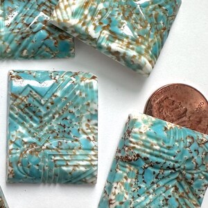 May include: A collection of rectangular ceramic tiles with a turquoise, brown, and white color scheme. The tiles feature a geometric pattern and a textured surface. A penny is included for size reference.