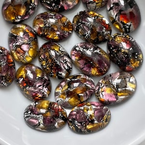Peut inclure: Assortiment de 15 cabochons en verre iridescent de forme ovale, avec un mélange de couleurs dorées, violettes et noires. Les cabochons mesurent environ 2,5 cm de long.