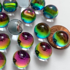 May include: A collection of glass marbles in various sizes and colors. Some marbles have a clear, iridescent finish with hues of purple, green, and gold. A penny is included for size comparison. The marbles are scattered on a white surface.
