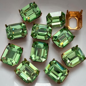 May include: A collection of rectangular, light green faceted glass stones set in gold-toned metal prong settings. Each stone features a clear, emerald-cut design with reflective surfaces, and one empty gold metal setting is visible among them.