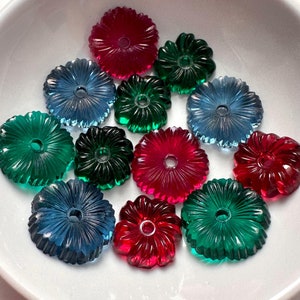 May include: A collection of translucent, flower-shaped beads in shades of red, blue, and green. Each bead features a central hole and radial, petal-like ridges. The beads are arranged in a cluster, showcasing their glossy finish and vibrant colors.