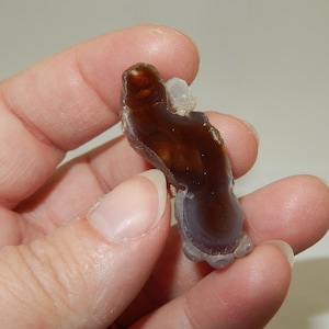 May include: A brown and purple agate with a white center. The agate is smooth and polished, and has a natural, organic shape.