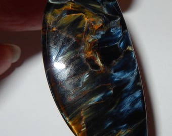 May include: A blue, gold, and brown tiger's eye cabochon gemstone with a smooth, oval shape.