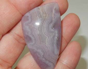 May include: A purple and white agate cabochon with a swirling pattern. The cabochon is shaped like a teardrop and has a smooth, polished surface.