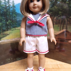 May include: A doll with blonde hair wearing a navy blue and white gingham sleeveless top with a sailor collar and a red tie. The outfit includes white shorts with red rickrack trim along the hem and red and white sneakers with white laces.