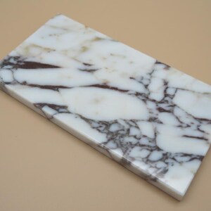 May include: A rectangular marble slab with a white base and dark brown veining. The polished surface has a natural stone pattern. The slab is likely used for decorative or functional purposes, such as a cutting board or serving tray.