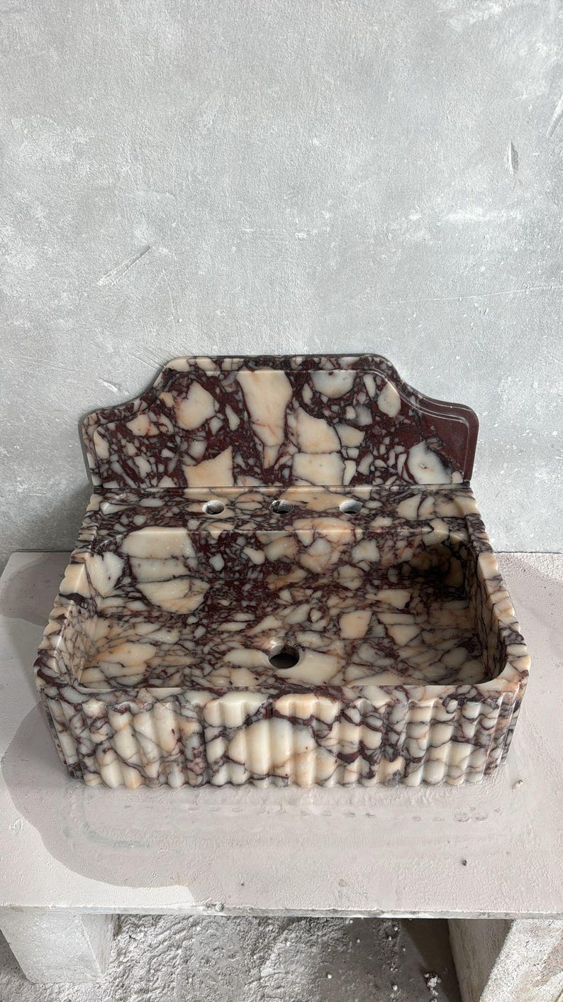 May include: A marble sink with a rectangular basin and a decorative backsplash. The sink features a pattern of burgundy and cream-colored veining. The front of the sink has a fluted design.