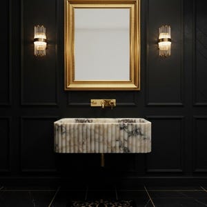 Puede incluir: Un lujoso cuarto de baño con un lavabo de mármol, un espejo con marco dorado y grifos dorados. Las paredes negras tienen paneles decorativos y la iluminación la proporcionan dos apliques de pared.