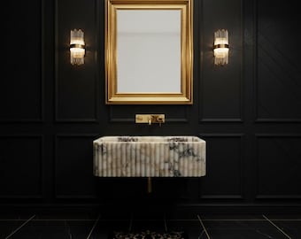 May include: A luxurious bathroom scene featuring a marble sink with vertical lines, a gold-framed mirror, and gold fixtures. The walls are black with decorative panels, and the lighting is provided by two sconces.