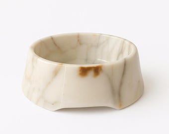 Puede incluir: Un cuenco color crema con efecto mármol y vetas marrones. El cuenco tiene forma octogonal con una amplia abertura y una base plana. El interior es liso y el exterior tiene un acabado pulido.