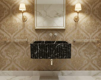 May include: A black marble sink with white veining is the focal point of this bathroom. The sink is mounted on a wall with ornate wallpaper. Two sconces flank a framed mirror above the sink, and a towel bar is visible.