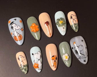 May include: A set of ten almond-shaped false nails with various designs. The nails feature cartoon characters, flowers, and glitter. Colors include light blue, peach, green, and orange. Some nails have 3D embellishments.