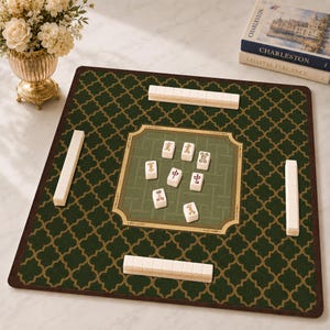 May include: A square mahjong mat featuring a dark green fabric surface with a gold quatrefoil pattern. The center has a lighter green woven-style square with seven white mahjong tiles and four rows of tiles placed along the edges of the mat.