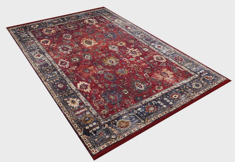 K&ouml;nnte beinhalten: Ein rechteckiger Teppich mit traditionellem Design. Der Teppich hat ein tiefrotes Mittelfeld mit floralen und geometrischen Mustern in Blau, Beige und Gold. Ein dunkelblauer Rand umrahmt das Design.