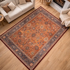 Pu&ograve; includere: Vista dall'alto di un tappeto rettangolare con un intricato motivo floreale. Il tappeto presenta un campo centrale arancione-rossastro caldo e un bordo blu scuro. Il design include elementi floreali e geometrici, creando un aspetto classico e invitante.