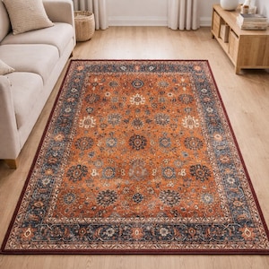 Pu&ograve; includere: Un tappeto con un intricato motivo floreale nei toni dell'arancione, blu navy e crema. Il tappeto ha un bordo rosso scuro ed &egrave; posato su un pavimento in legno, aggiungendo calore e stile alla stanza.