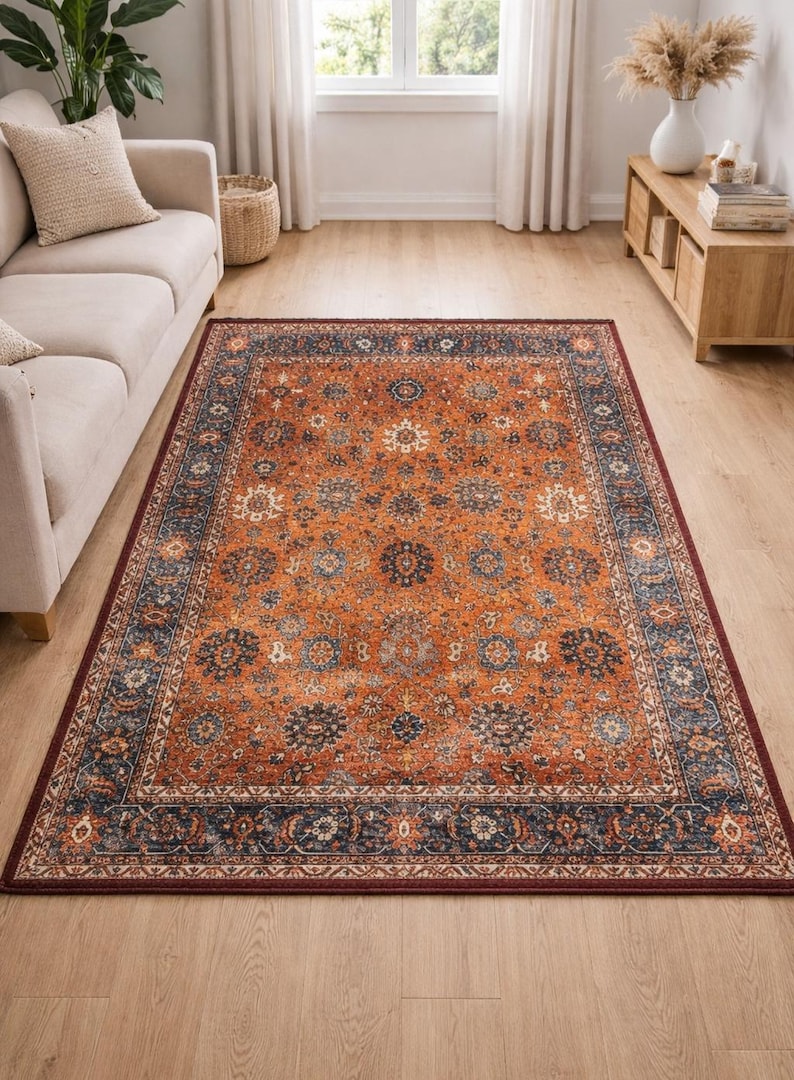 Pu&ograve; includere: Un tappeto con un intricato motivo floreale nei toni dell'arancione, blu navy e crema. Il tappeto ha un bordo rosso scuro ed &egrave; posato su un pavimento in legno, aggiungendo calore e stile alla stanza.