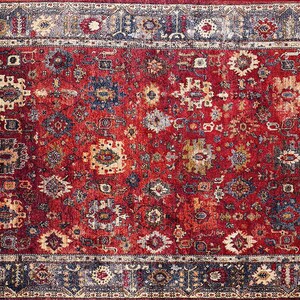 K&ouml;nnte beinhalten: Ein rechteckiger Teppich mit einem roten Mittelfeld und einem detaillierten Rand. Der Teppich weist ein sich wiederholendes Muster aus floralen und geometrischen Designs in Blau-, Creme- und Goldt&ouml;nen auf. Der Rand ist dunkelblau mit Creme- und Goldakzenten.